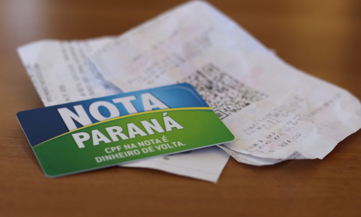 Foto mostra cartão do Nota Paraná ao lado de nota fiscal sobre mesa de madeira; imagem faz alusão à moradora que ganhou R$ 100 mil em sorteio