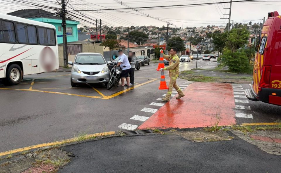 foto do acidente com carro que deixou o motociclista ferido em curitiba. na imagem aparece duas pessoas empurrando a moto, o carro envolvido na batida e a ambulância do siate