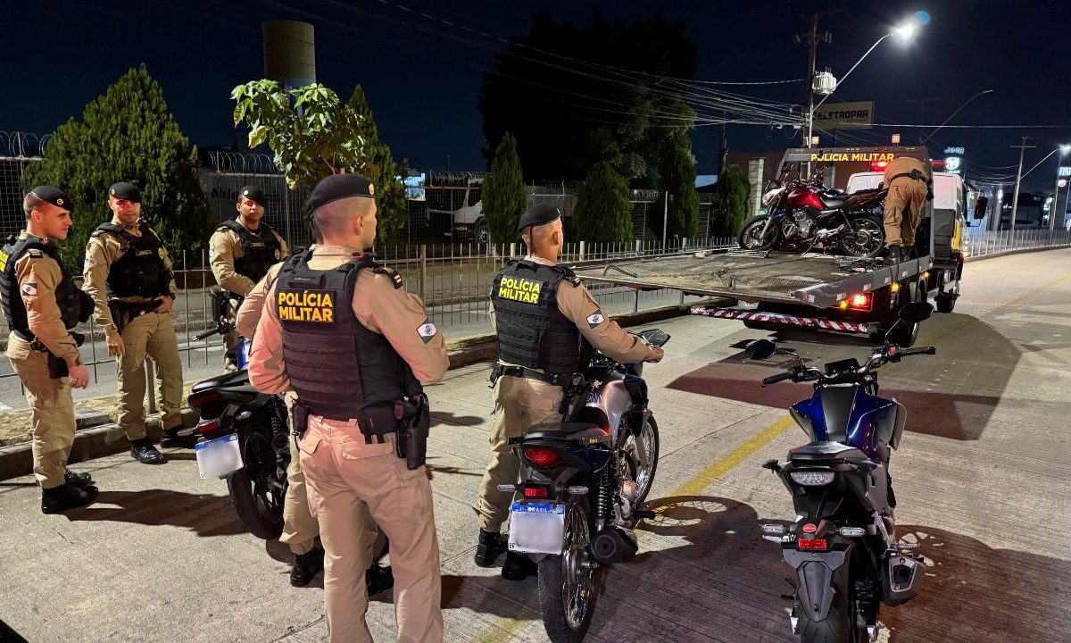 Foto mostra policiais militares do BPTran recolhendo motos e colocando sobre caminhão-guincho durante operação, no bairro Parolin, em Curitiba. Motociclistas são multados e têm motos apreendidas.