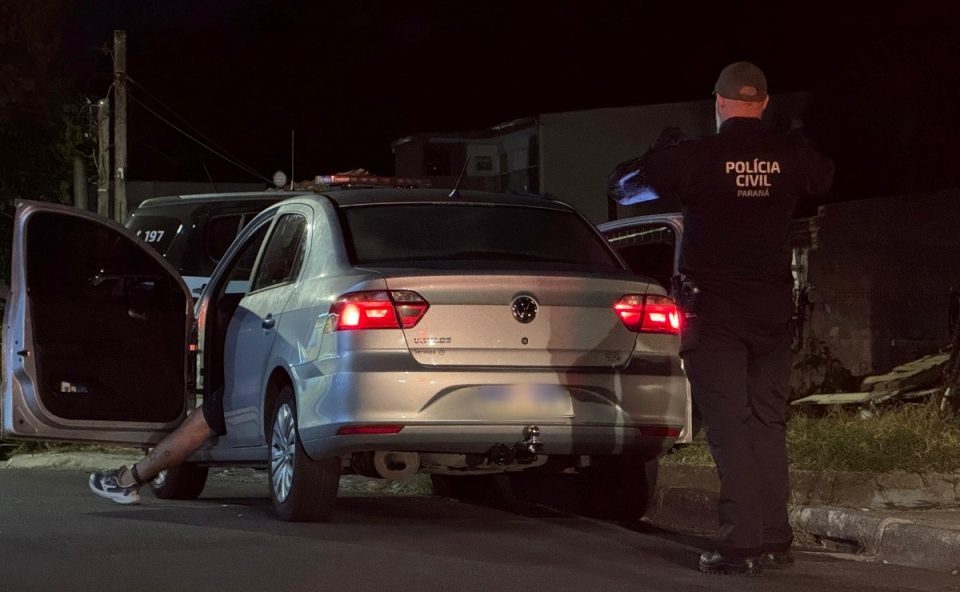 Imagem mostra a perna de um motorista de aplicativo executado a tiros em Curitiba para fora de um Voyage estacionado em frente a uma distribuidora no bairro Barreirinha. A tornozeleira eletrônica e tatuagens da vítima estão visíveis. Ele foi morto dentro do veículo enquanto estava com três filhos, que não ficaram feridos, após um atirador se aproximar e disparar contra o carro.