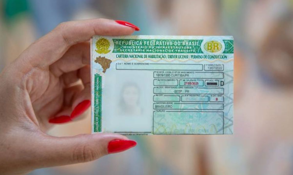 Imagem mostra uma mão de uma mulher com unha pintada de vermelho segurando uma CNH. Foto ilustrativa para mudanças na CNH para motoristas da categoria B.