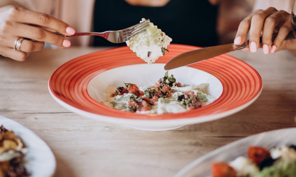 Imagem ilustrativa para mulher que chamou a polícia após o marido se negar a preparar o jantar. Foto mostra uma mão feminina comendo. A comida está em um prato fundo com borda salmão.