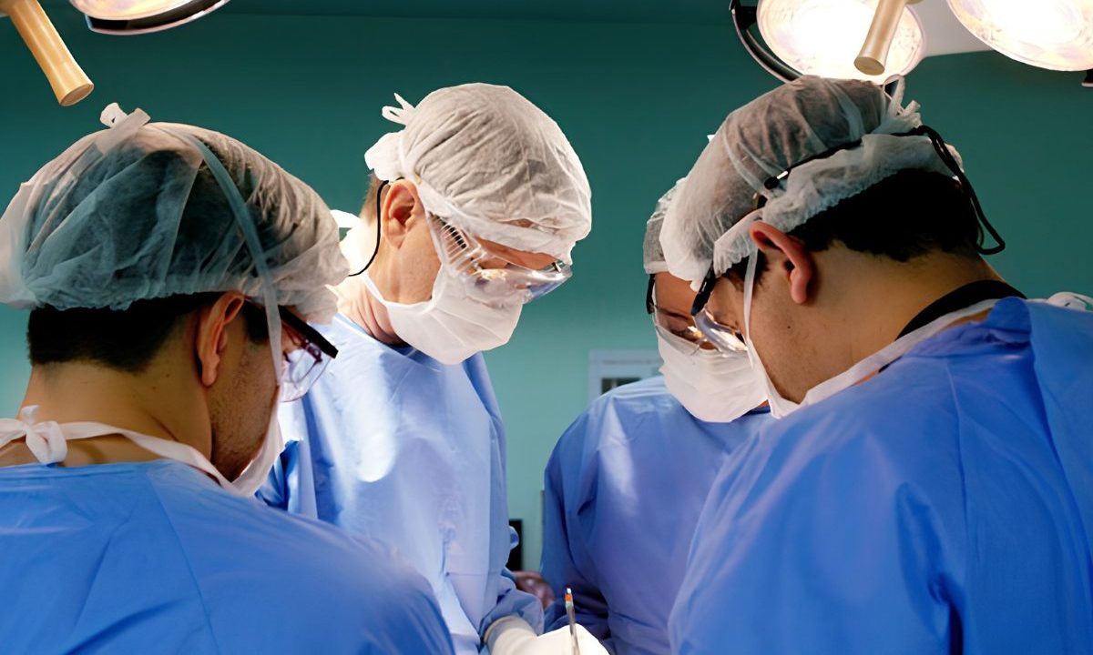 Equipe médica realiza procedimento cirúrgico em hospital, utilizando equipamentos e roupas esterilizadas.