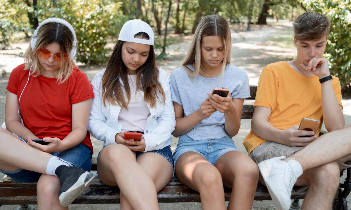 Foto de jovens mexendo no celular, um ao lado do outro; imagem usada para ilustrar o que significa six-seven e farmar aura
