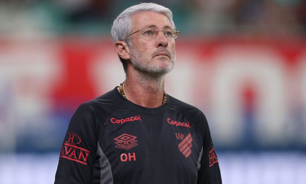 Odair Hellmann, técnico do Athletico, em pé à beira do campo durante partida, usando uniforme preto do clube e observando o jogo com expressão concentrada