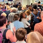 Foto de passageiros presos em aeroporto. Eles estão desorganizados e espaçados, sem uma fila definida.
