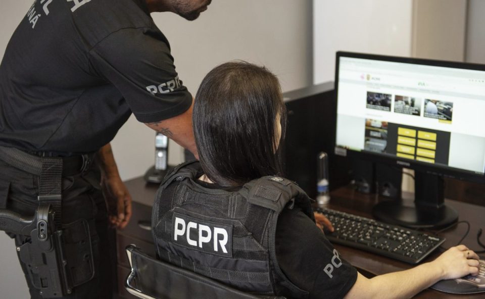 Agentes da Polícia Civil do Paraná analisam conteúdo em computador durante investigação de crimes virtuais.