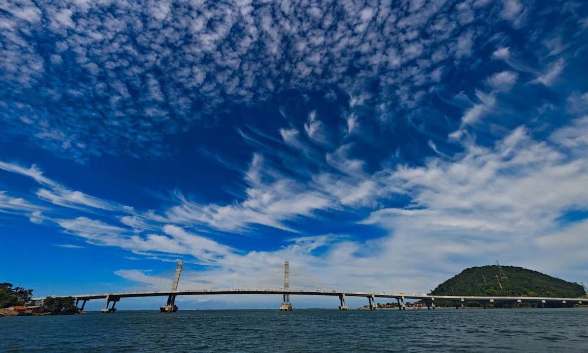 Foto mostra Ponte de Guaratuba de longe, em dia azul