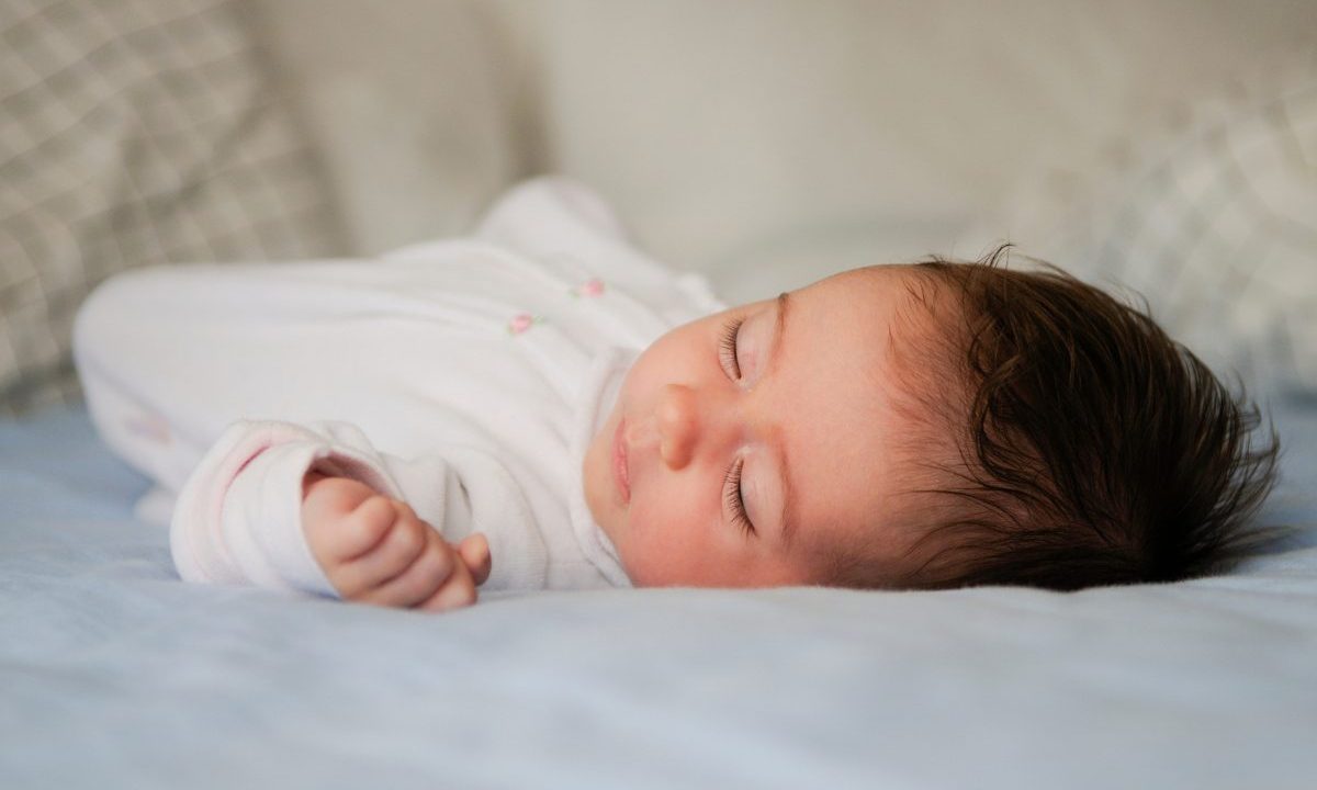Bebê dormindo de lado em superfície plana, com a cabeça apoiada em um dos lados indicando melhor posição para o sono.