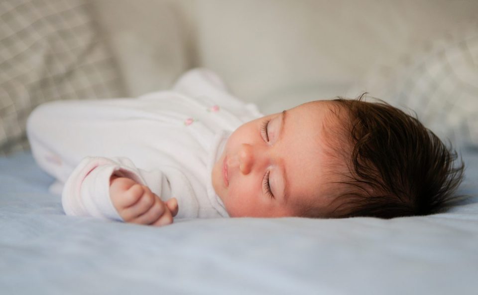 Bebê dormindo de lado em superfície plana, com a cabeça apoiada em um dos lados indicando melhor posição para o sono.