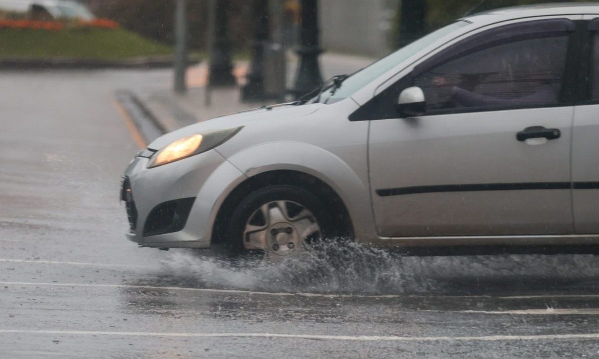 Imagem ilustrativa da previsão do tempo em Curitiba mostra um carro em uma rua com água de chuva. Previsão indica alta probabilidade de chuva nesta quinta-feira. O carro é cinza.