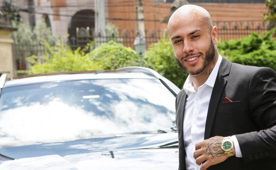 Cristiano Galego, conhecido como Rei das Loiras, é alvo de investigação e mandado de busca e apreensão. Imagem mostra o cabeleireiro com terno preto, relógio de ouro e camisa branca. Ele é careca e tem barba e bigode.
