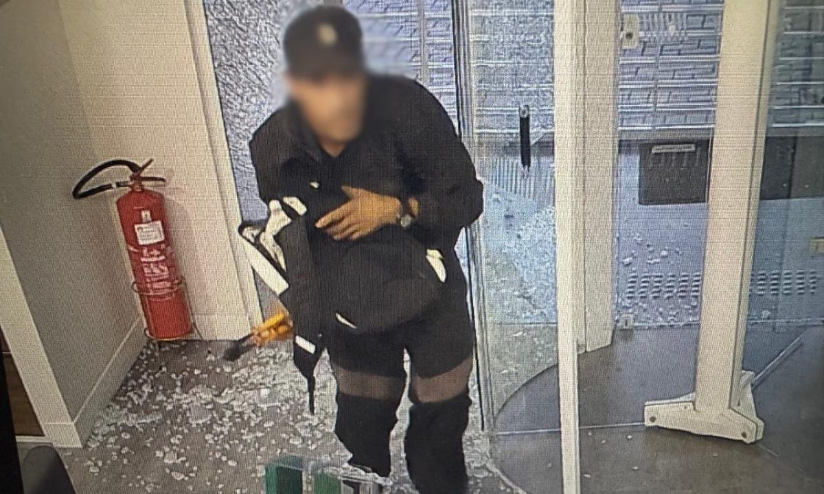 Suspeito de arrombar agências bancárias em Curitiba é preso. Imagem mostra o suspeito com moletom preto e boné. Atrás aparecem vidros estilhaçados no chão após o arrombamento em uma agência bancária. Há também um extintor na foto.