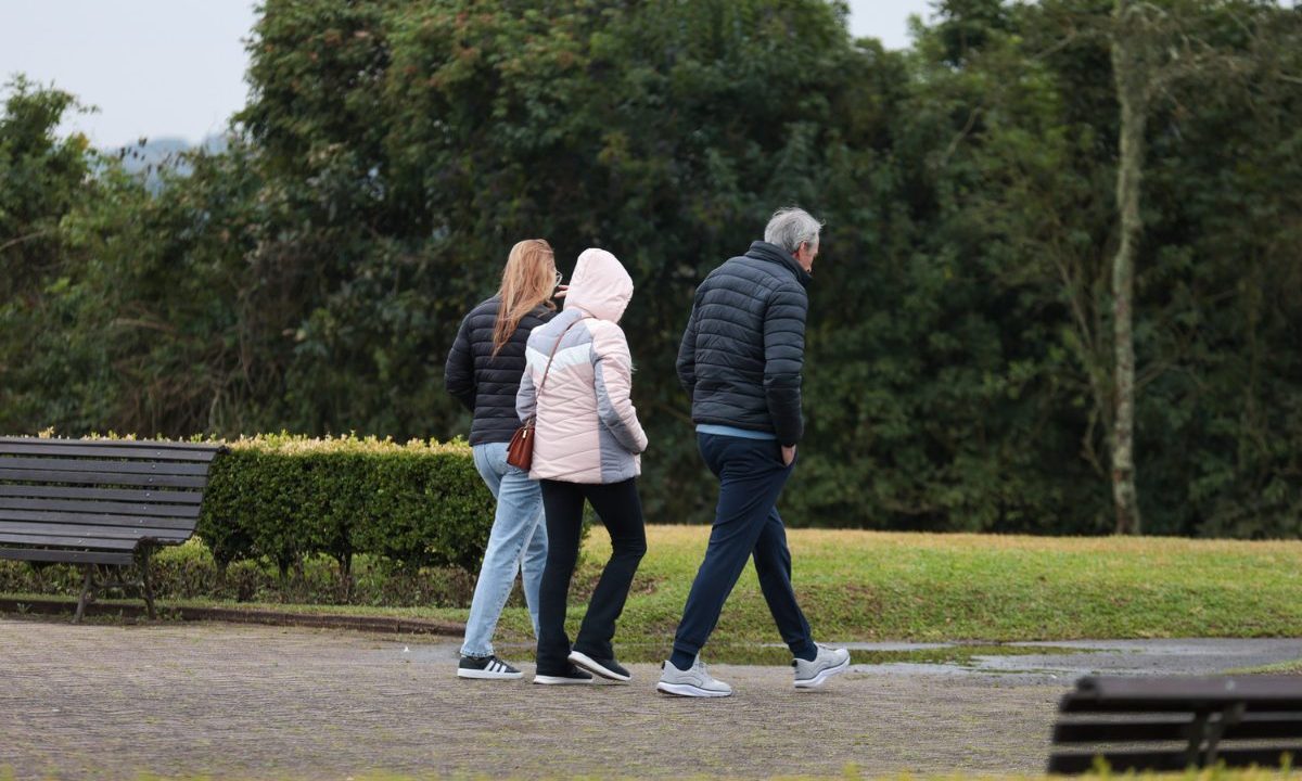 Foto ilustrativa para a previsão do tempo em Curitiba nesta sexta-feira. Imagem mostra uma família com roupa de frio andando em um parque, perto de um gramado. São três pessoas. Um homem e três mulheres.