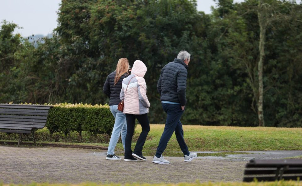 Foto ilustrativa para a previsão do tempo em Curitiba nesta sexta-feira. Imagem mostra uma família com roupa de frio andando em um parque, perto de um gramado. São três pessoas. Um homem e três mulheres.
