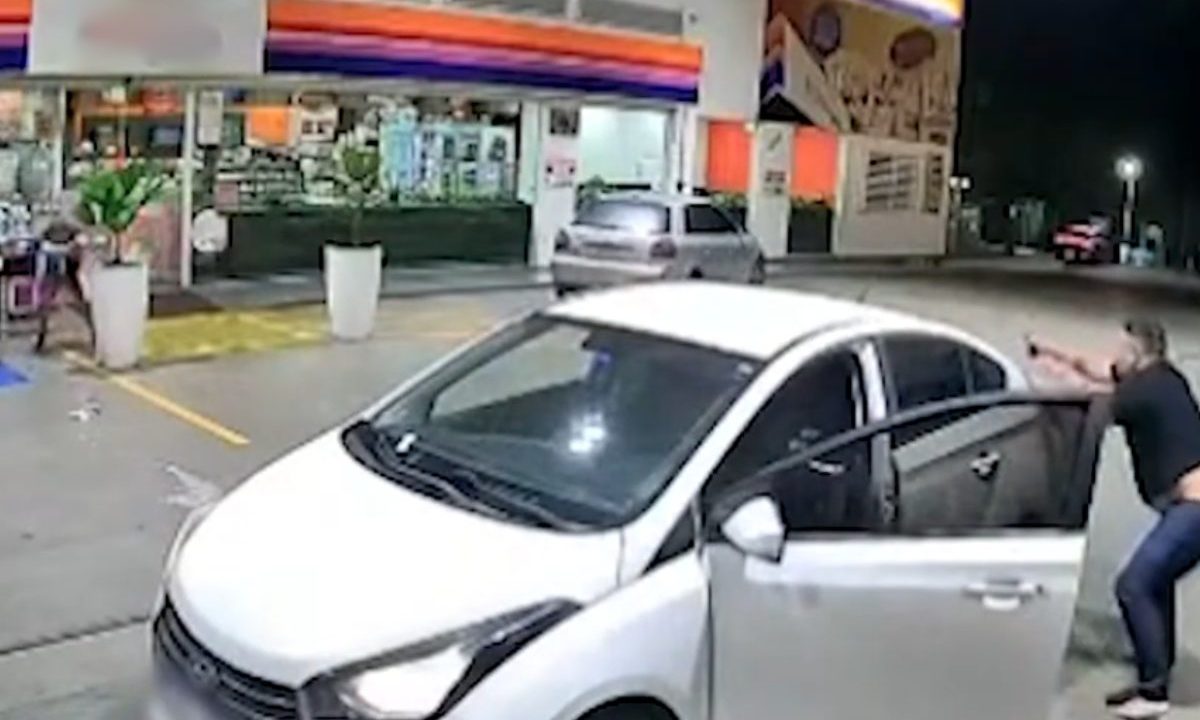 Dois homens armados apontam armas um para o outro em frente a uma loja de conveniência em posto de combustíveis, em imagem de câmera de segurança.