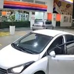 Dois homens armados apontam armas um para o outro em frente a uma loja de conveniência em posto de combustíveis, em imagem de câmera de segurança.
