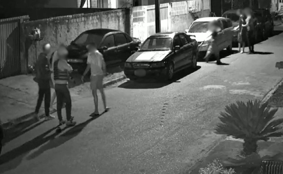 Imagem mostra parte do sequestro em Fazenda Rio Grande. Foto é uma captura de tela do vídeo do sequestro. Imagem mostra os criminosos abordando as duas vítimas em uma rua. Há carros estacionados e o restante da quadrilha aguarda ao fundo da foto.