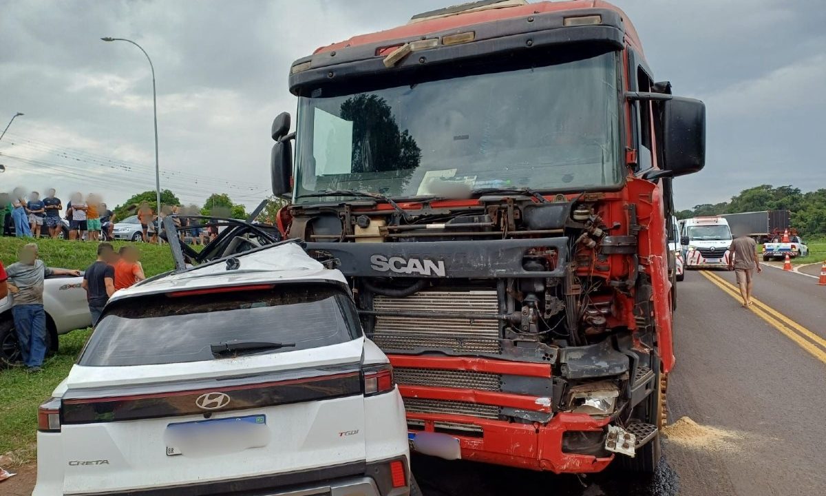 Foto mostra carro branco destruído por caminhão vermelho após ser arrastado em acidente que matou criança de 7 anos no Paraná. Testemunhas e curiosos acompanham os desdobramentos do atendimento às vítimas