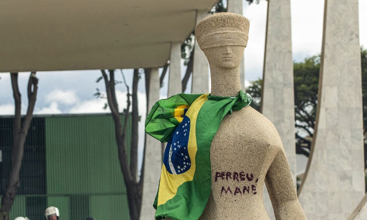 Estátua da justiça em frente ao STF com bandeira do Brasil amarrada no pescoço e "perdeu mané" pixado na barriga pela Débora do Batom, que teve revisão de pena negada por Moraes