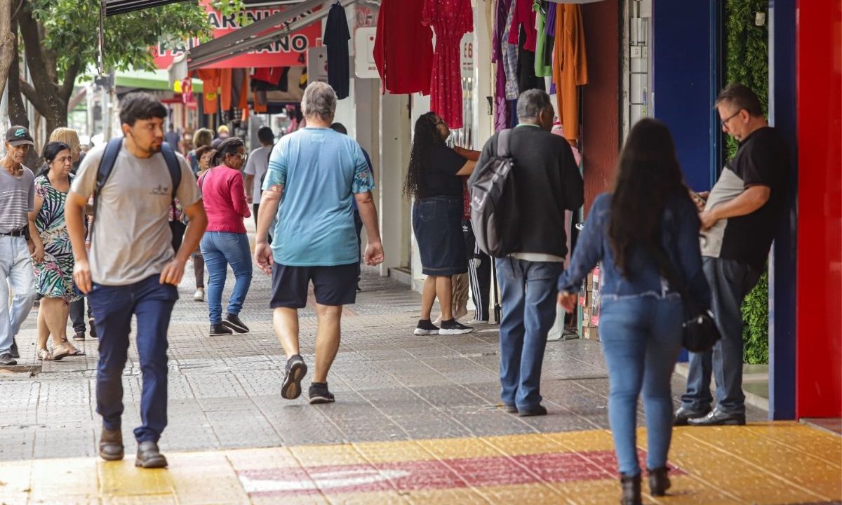 Movimentação de pedestres em frente a lojas de roupas no centro da cidade, ilustrando o impacto do fim da taxa das blusinhas no comércio local.