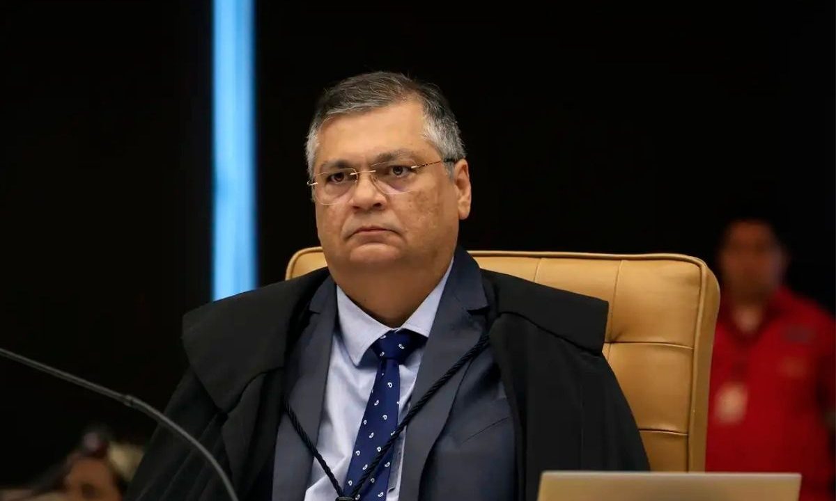 O ministro do STF Flávio Dino sentado em sua cadeira no plenário, vestindo toga preta e gravata azul. Ele é o relator da investigação sobre o uso de emendas no filme de Bolsonaro.
