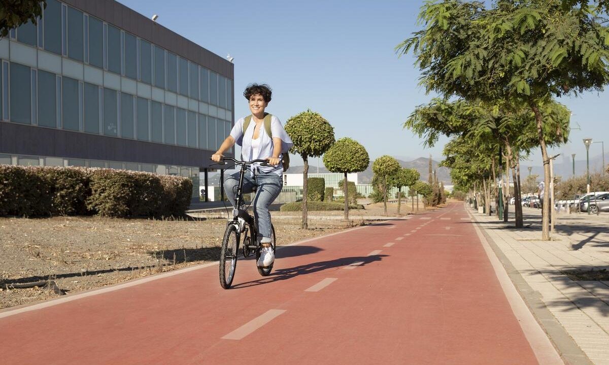 Mulher jovem e feliz andando de bicicleta em uma ciclovia, elemento urbanístico que pode eliminar o acostamento com nova norma