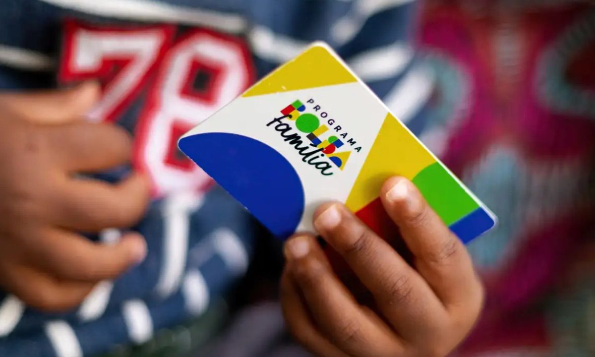 Cartão do Bolsa Família na mão de uma criança representando os benefícios de programas sociais recebidos no Paraná
