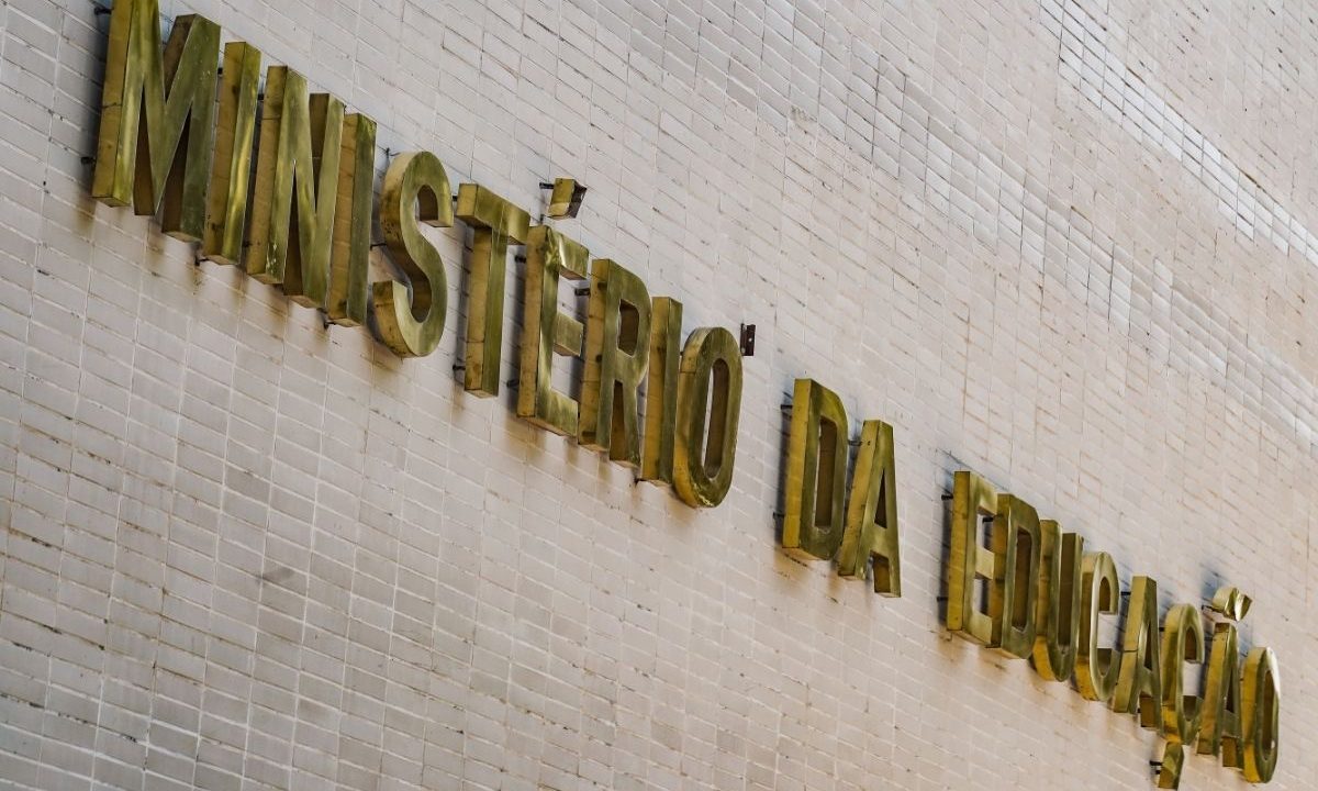 Foto em ângulo diagonal da fachada do prédio do Ministério da Educação, exibindo as letras douradas em relevo com a inscrição "MINISTÉRIO DA EDUCAÇÃO" fixadas sobre uma parede de azulejos brancos.