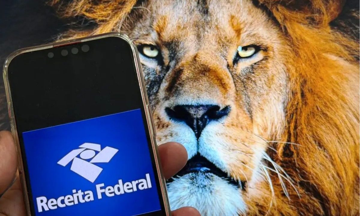 Smartphone exibindo o logotipo azul do aplicativo da Receita Federal em primeiro plano, com a imagem da cabeça de um leão ao fundo, ilustrando o prazo do imposto de renda.