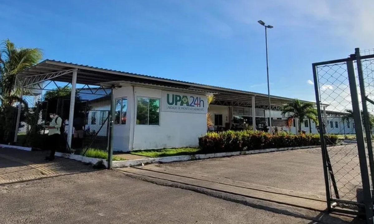 Unidade da UPA em Trapiche, com grama, arbustos, céu azul e cercada com grades. No registro também aparece um homem com máscara na porta da unidade
