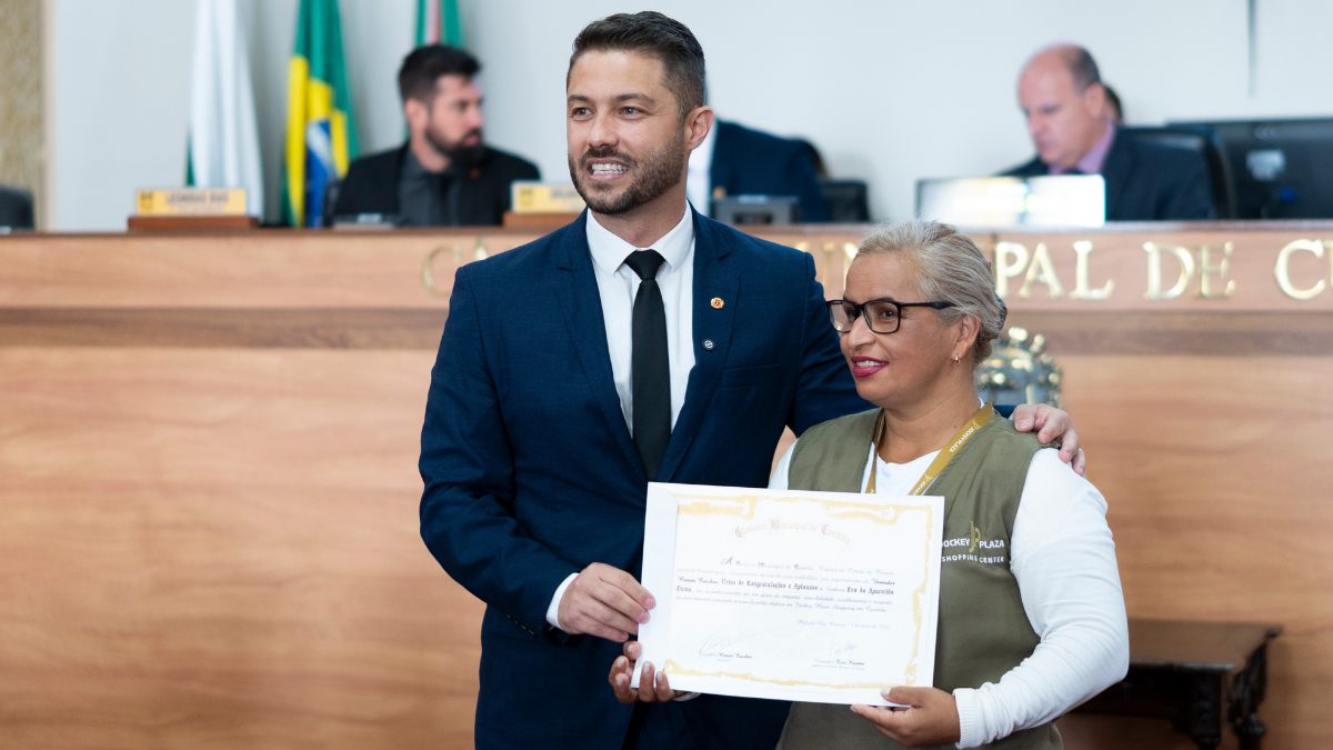 O vereador Renan Ceschin entrega diploma de menção honrosa para a colaboradora Eva Aparecida Dama, que usa o colete do Jockey Plaza Shopping.