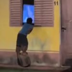 Menino Mael apoiado em um toco de madeira para assistir televisão pela janela da vizinha em Ubajara, Ceará.