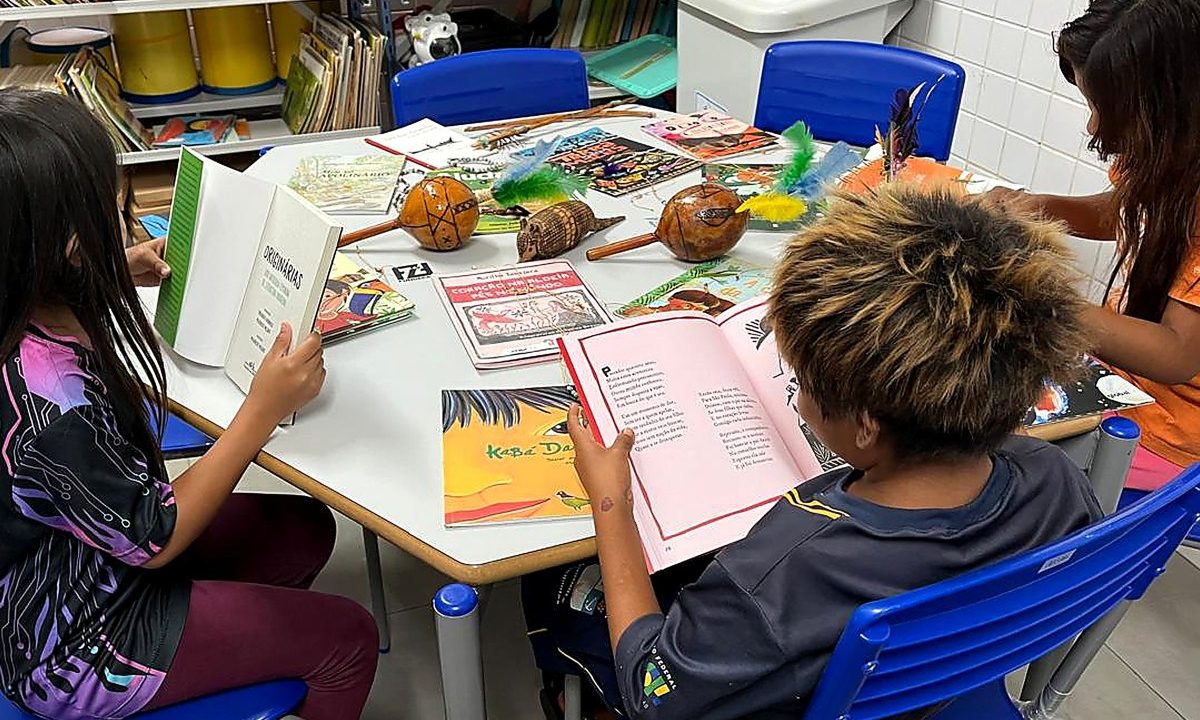 Crianças sentadas em volta de uma mesa, lendo. Imagem ilustrativa para matéria sobre o Paraná liderar o país com o maior índice de escolas com biblioteca.