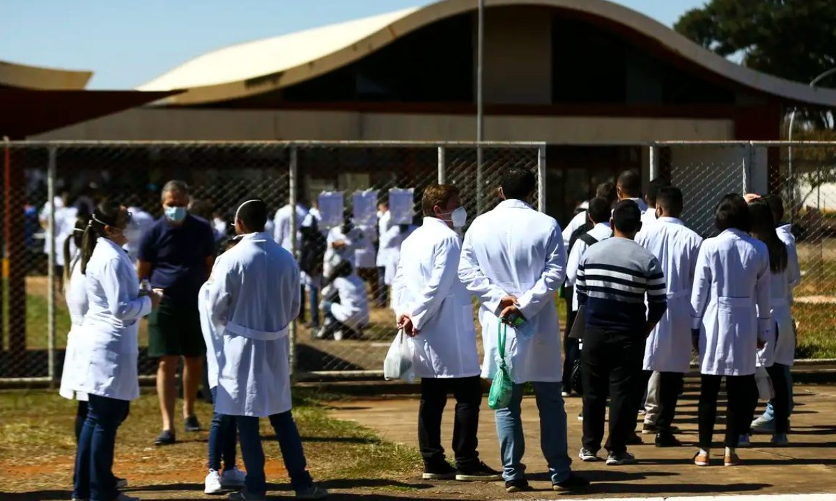 Pessoas de jaleco branco de costas em uma fila indiana. Imagem ilustrativa, para matéria sobre: Revalida 2026/1: nota de corte da primeira fase da prova é estabelecida