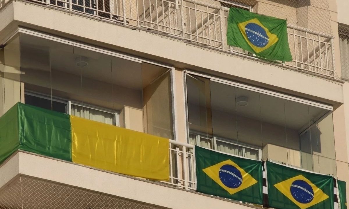 Fachada de prédio residencial mostrando sacadas de apartamentos estendendo a bandeira do brasil na grade de proteção, ilustrando o debate sobre regras de condominio.