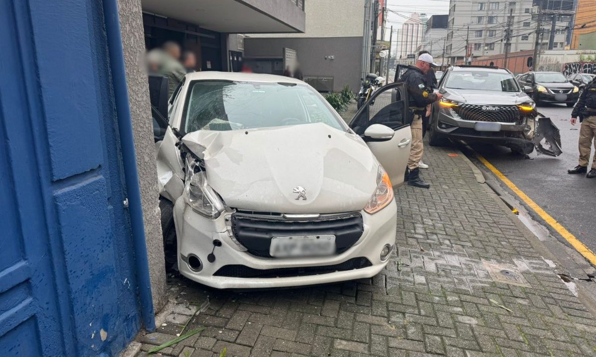 Imagem mostra o acidente no Centro de Curitiba, provocado por um jovem de 19 anos sem CNH. Foto mostra um Peugeot branco com a frente destruída. Airbags foram acionados. Atrás, aparece o veículo Haval com a frente batida também. Policiais estavam no local da ocorrência.