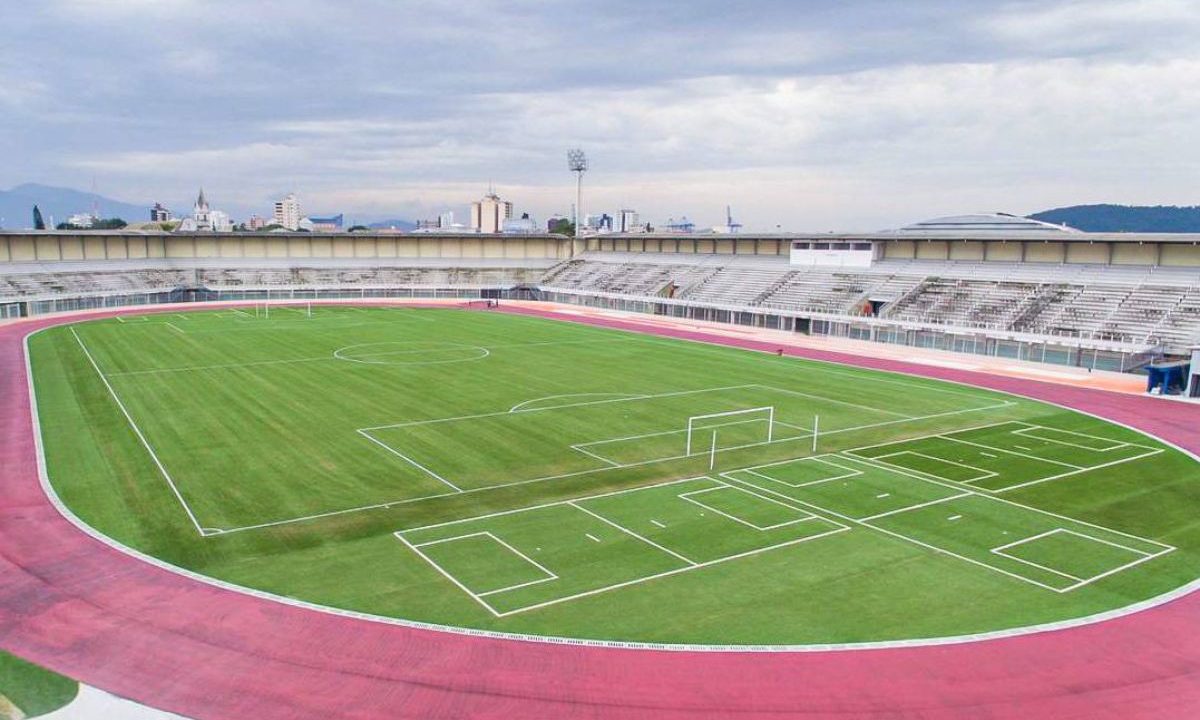 Imagem mostra uma visão ampla do estádio Gigante do Itiberê, em Paranaguá. O gramado aparece vazio, cercado por pista de atletismo vermelha e arquibancadas cinzas ao fundo sob céu nublado. Será o local de Araucária x Paraná Clube.