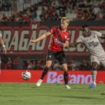 A imagem mostra um lance do confronto entre Atlético-GO e Athletico no estádio Antônio Accioly. No centro da foto, o atacante Kevin Viveros, do Furacão, disputa a posse de bola com um jogador da equipe goiana. Outros atletas acompanham a jogada ao redor, enquanto a torcida aparece ao fundo nas arquibancadas.