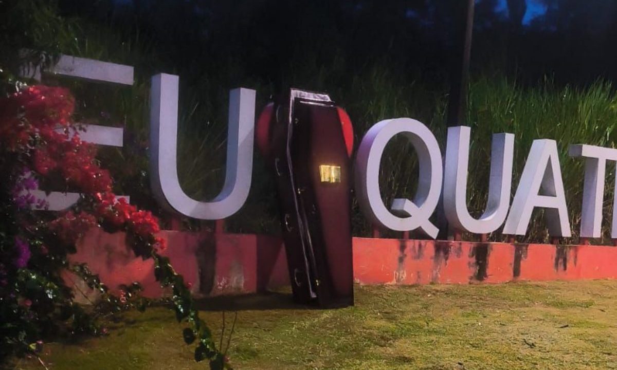 Imagem mostra caixão em frente a letreiro de cidade.