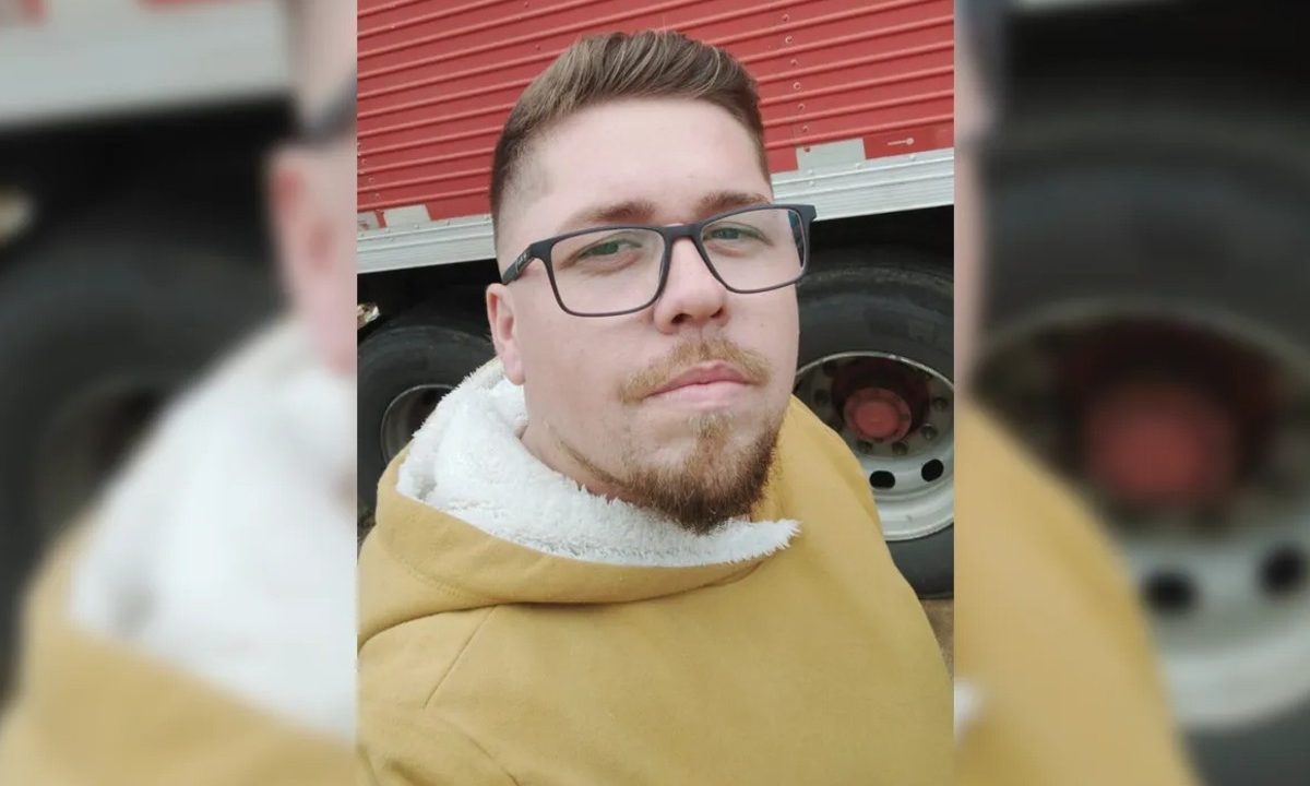 Na foto, o caminhoneiro Alexandre Freitas Bispo aparece posando para selfie ao lado de um caminhão vermelho. Ele tem o cabelo loiro escuro, olhos claros, barba com cavanhaque e pele branca. Ele usa uma blusa amarelo queimado. Caminhoneiro morreu após despencar de barranco e ficar 47 dias internado na UTI