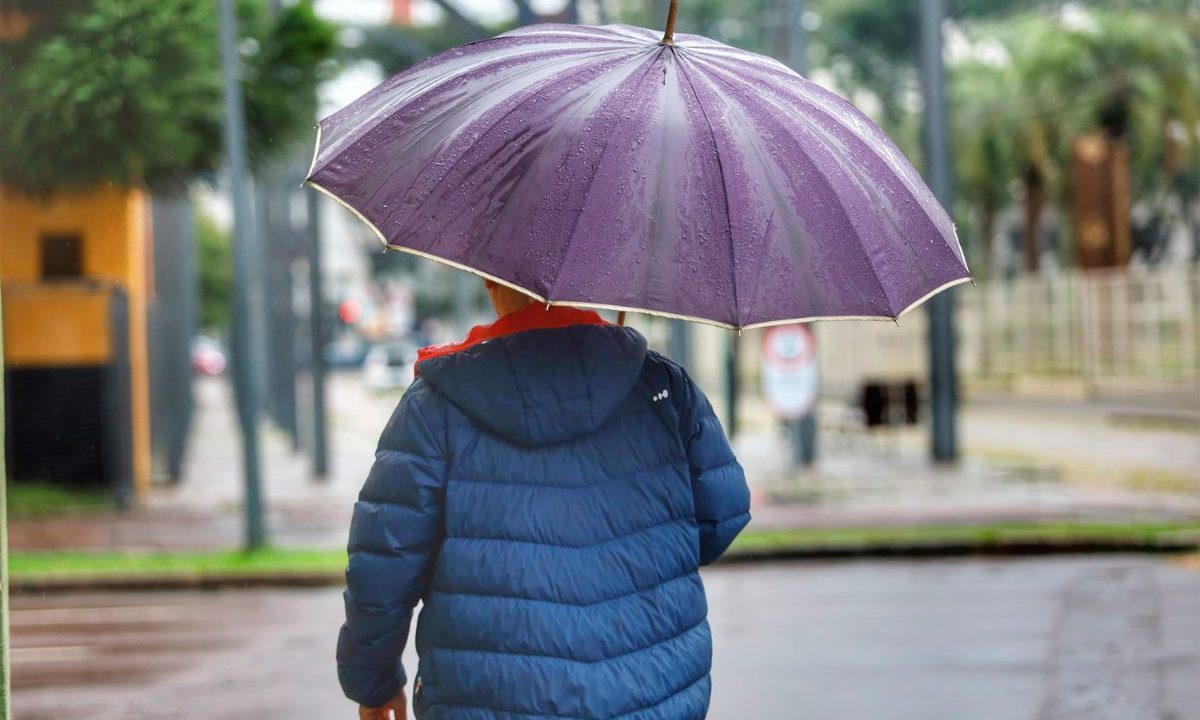 Pessoa caminha com guarda-chuva em rua de Curitiba durante dia chuvoso provocado pela frente fria no Paraná