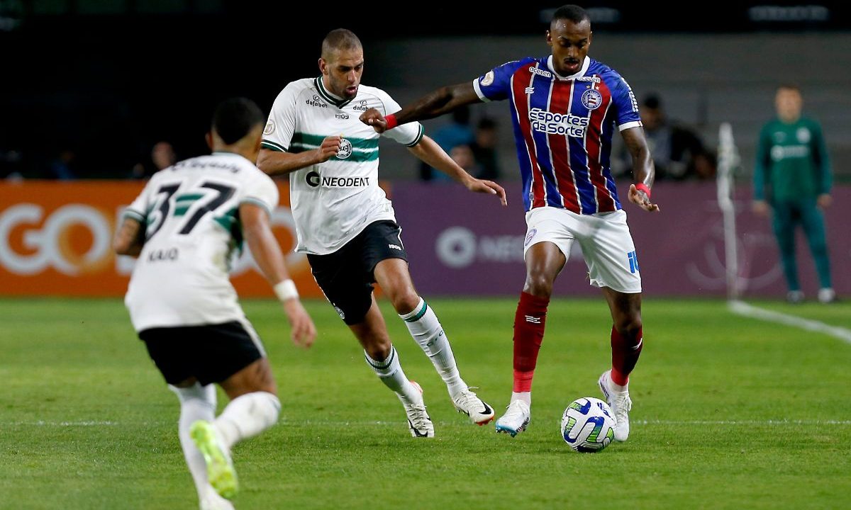 Dois jogadores de Coritiba e Bahia disputam a posse de bola durante partida do Campeonato Brasileiro de 2023. O atleta do Tricolor conduz a bola enquanto jogadores do Coxa pressionam a marcação em campo.