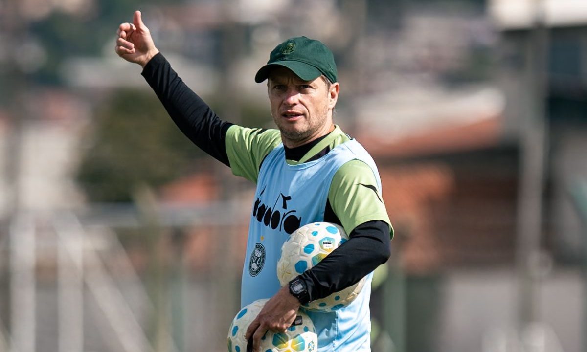 Imagem mostra o técnico Fernando Seabra durante treinamento do Coritiba. O treinador aparece segurando bolas e gesticulando no gramado do CT da Graciosa, usando uniforme de treino verde e preto do clube.