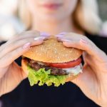 Foto de uma mulher segurando um hambúrguer, representando o consumo do lanche em Curitiba.