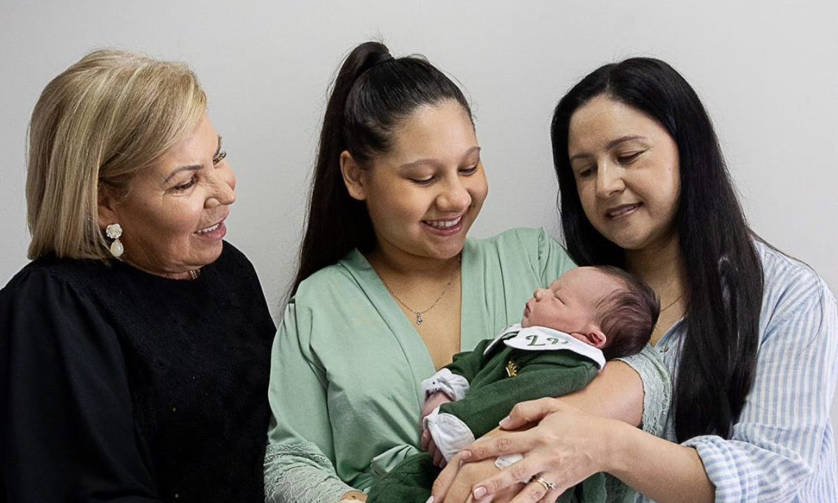 Bruna, a filha e a mãe observam e seguram o recém-nascido da família em momento de carinho entre três gerações conectadas por maternidade de curitiba