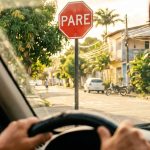 motorista brasileiro dirige em direção a placa de parada obrigatória em via urbana representando infrações de trânsito comuns