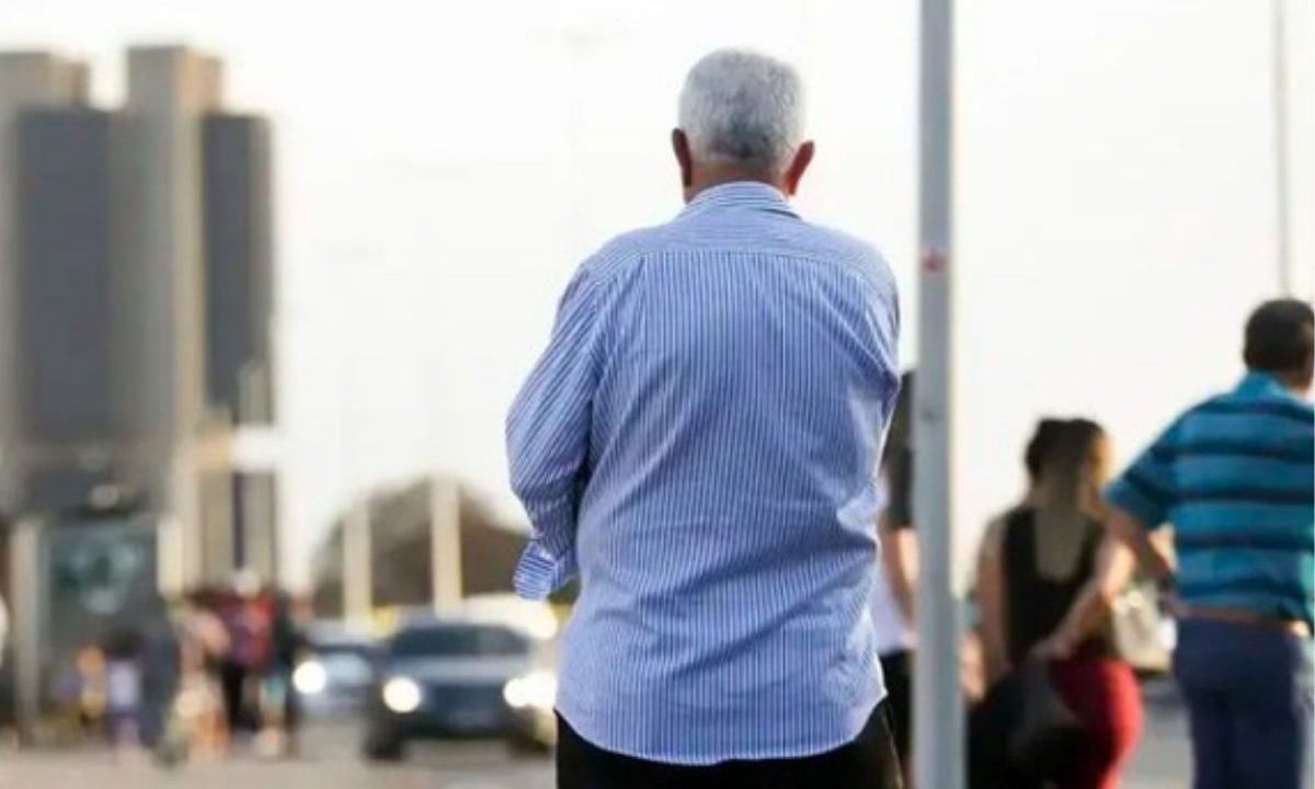 INSS começará a enviar notificações pelo WhatsApp para beneficiários que precisam regularizar a prova de vida. A imagem mostra o um idoso, de camisa azul, em uma calçada, olhando para frente.