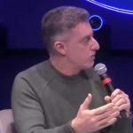 Imagem mostra o apresentador Luciano Huck detonando o Bolsa Família. Ele usa blusa verde musgo e segura um microfone. Ele tem cabelo grisalho.
