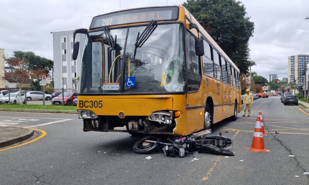 Foto de uma motocicleta debaixo de um ônibus do transporte coletivo após acidente que deixou um motociclista ferido no bairro Ahú, em Curitiba.